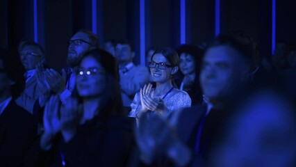 Young Woman Sitting in a Crowded Audience at a Business Conference. Female Attendee Cheering and Clapping After a Motivational Keynote Speech. Auditorium with Young Successful Businesspeople.