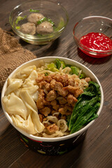 Chicken noodles in white bowl and wooden chopsticks on natural background with chicken pieces, green mustard greens, meatballs, boiled dumplings, sauce. Indonesian Chicken Noodles