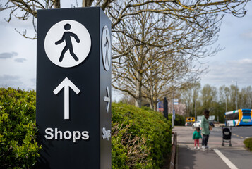 Large directional signage post with arrow and person walking icon pointing along path towards shopping retail area.