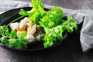 Thai Steamed Pork Dumplings served in a black plate with lettuce and coriander in a restaurant in Thailand.