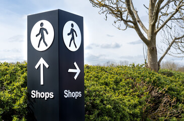 Large black and white free standing directional sign with person symbol and arrows pointing to shops