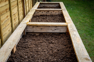 Close up of large wooden planter vegetable box containers in backyard garden filled with soil ready...