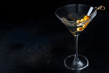 Martini, a glass with spicy olives on a toothpick, on a black background. Alcoholic drink with copy space