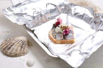 Sandwich with herring and pickled onion, decorated with edible flowers, in a takeaway box. Fish appetizer.