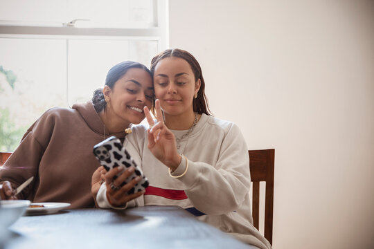 Smiling, cool young adult sisters taking selfie with smart phone