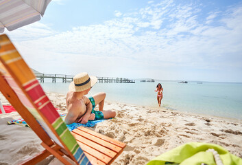 Girlfriend gesturing to boyfriend relaxing on sunny summer ocean beach