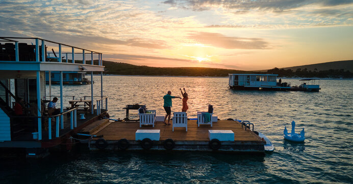 Carefree couple dancing on houseboat patio on lake at sunset
