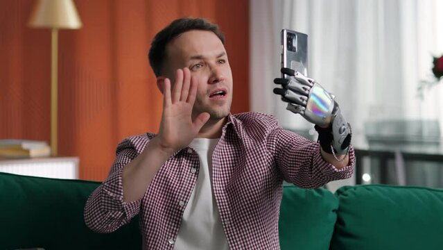 Young man with bionic arm prosthesis taking selfie on smartphone at home