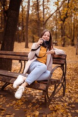 Beautiful young woman photographer with a camera in the autumn park not a bench. Smiling girl enjoys the autumn weather, lifestyle concept