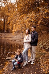 happy family with a child on an autumn walk in a city park with a lake, feeding ducks, family fun