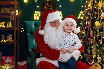 Happy cute little boy sitting with Santa Claus near Christmas tree. New Year concept 