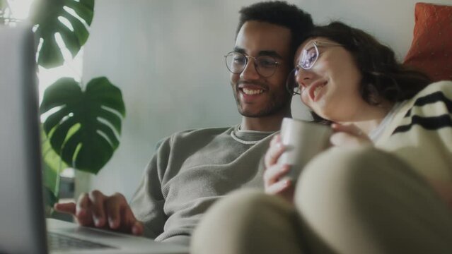 Young romantic couple browsing the Internet on laptop, smiling and talking while browsing the web on laptop