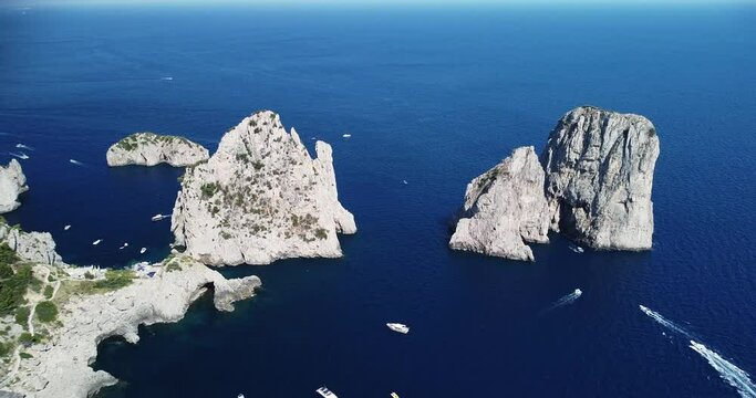 Aerial drone footage of the Tyrrhenian sea coast of Capri, Italy. Beautiful rocky cliffs, transparent blue water, boats moving and floating, mountains inside the ocean. Major tourist attractions 
