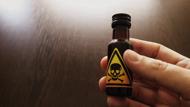 hand holding a small bottle of poison with a yellow toxic sign represented by a skull and two bones icon - dangerous concoction for a poisoning