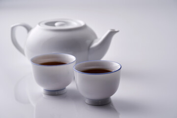 two tea cups and teapot against with background with reflection