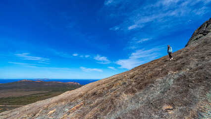 brave backpacker girl descends from frenchman peak in cape le grand national park in western australia, hiking and climbing a mountain with a backpack