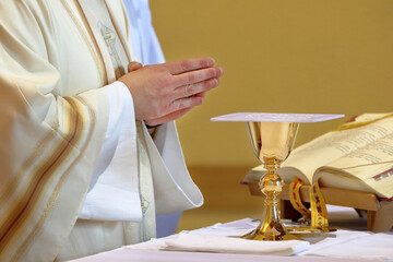 Chalice on the altar and priest celebrating mass in the background