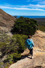 Obraz premium brave backpacker girl descends from frenchman peak in cape le grand national park in western australia, hiking and climbing a mountain with a backpack
