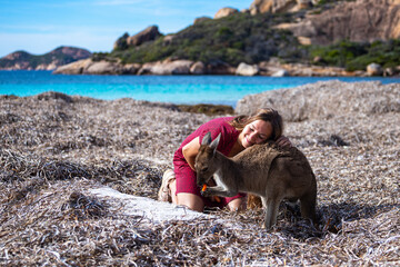 girl in dress feeds, petts and cuddles wild kangaroo on lucky bay beach in west australia; paradise...