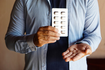 Closeup man holds silver aluminum blister packages of tablet pills medicine. Concept : Health care, health problem, sickness and remedy. Basic self take care at home when get sick.    