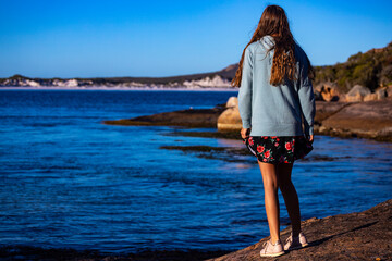 a beautiful long-haired woman in a skirt walks at sunset on the rocks by the ocean in western australia, a gorgeous beach with white sand and turquoise water in cape le grand national park near espera