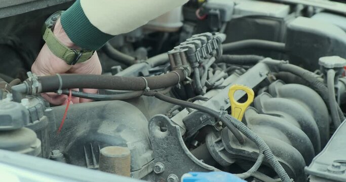 Car engine repair. The hands of an auto mechanic unscrew the bolts to get to the car spark plugs. Close-up, side view.