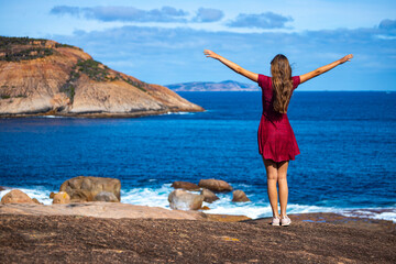 girl in a dress stands on rocks by the ocean in western australia; beautiful paradise bays in cape le grand national park, near esperance, australia