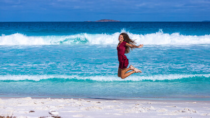 a beautiful girl in a red dress jumps for joy on a paradise beach in western australia, a gorgeous beach with white sand and turquoise water in cape le grand national park near esperance