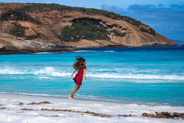 A long-haired girl in a dress dances, runs and fools around on a paradise Australian beach; white...