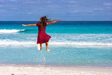 a beautiful girl in a red dress jumps for joy on a paradise beach in western australia, a gorgeous beach with white sand and turquoise water in cape le grand national park near esperance