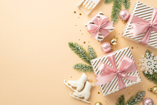 Christmas concept. Top view photo of gift boxes gold and pink baubles ice skates sledge snowflake ornaments spruce branches in snow and confetti on isolated pastel beige background with copyspace