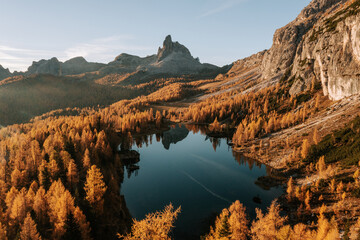 Erste Sonnenstrahlen am Lake Fedare / Lago di Federa in den Belluner Dolomiten zum Sonnenaufgang. Es ist Herbst und der Wald am See leuchtet gelb. Sonnenaufgang Dolomiten 12