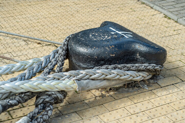 A close-up of a powerful bitts on the pier on which several marine ropes are fixed. Fastening to which ships are attached near the shore.