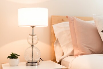 Beautiful lit lamp with a small plant on a nightstand next to the bed