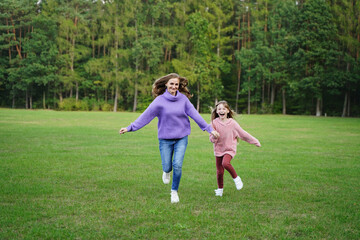 Naklejka premium Happy mom and daughter run outdoors. Joyful girl and woman have fun together. Family vacation in nature