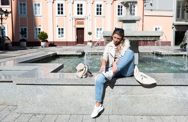 Young woman sitting at the town square on the water fountain cleaning and rubbing dog or pigeon...