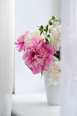 A view of a bouquet of pink and white peonies standing in a vase on the window. Concept background, flowers, holiday