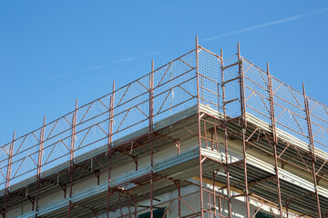 Metal scaffolding with protective grid for the renovation of the roof of the building and restoration of the plaster facade of an old building