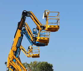 Row of aerial working platforms of cherry picker,  side by side against blue sky