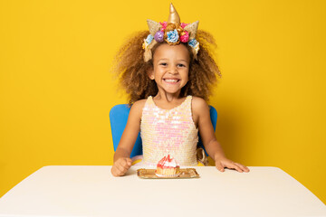 Cute child girl in unicorn headband celebrates birthday party over yellow background.