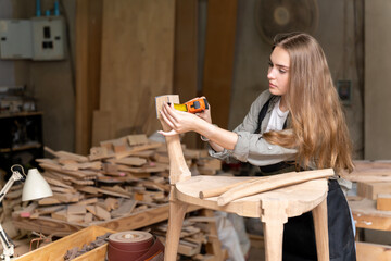 A female carpenter assembling a chair she had designed and built. At the furniture factory found inside her house
