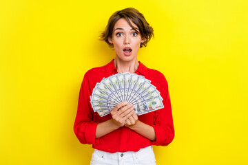 Portrait of impressed gorgeous woman with bob hairdo dressed red shirt hold dollars open mouth isolated on yellow color background