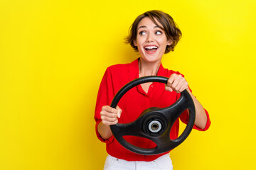 Photo of excited impressed girl with bob hairstyle wear red shirt hold steering wheel look empty space isolated on yellow color background