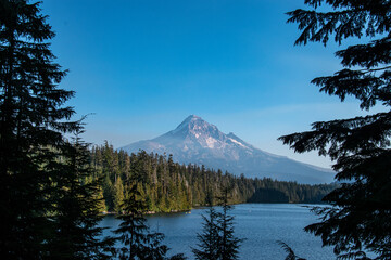 Mt Hood rises in the distance over Lost Lake in Oregon mid-afternoon.  The blue lake and green pine trees from the majestic mountain. 