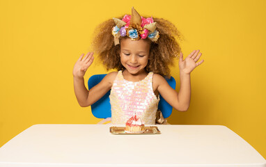 Cute child girl in unicorn headband celebrates birthday party over yellow background.