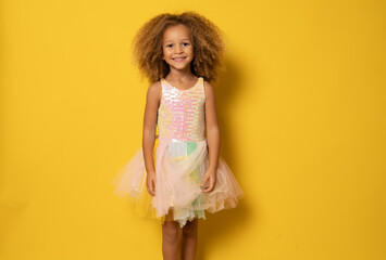 Cute child girl in elegant tulle dress celebrates birthday party over yellow background.