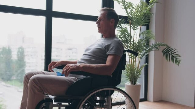 Senior disabled man sitting on the wheelchair near the window in the hospital