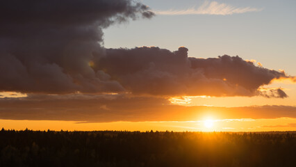Sun over the woods horizon. Dramatic scenery sunset landscape panorama with warm vivid sunlight from behind the clouds