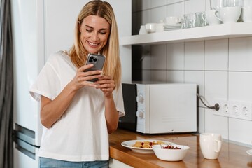 Happy woman laughing and using cellphone while having breakfast at home