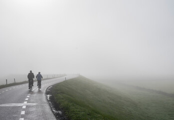 Obraz premium couple on bicycle rides in mist on dike near river rhine in holland